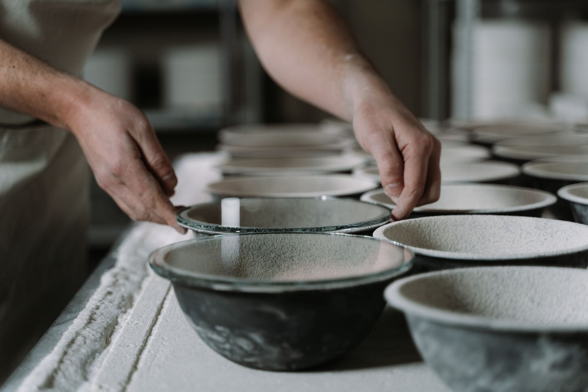 Handmade ceramic bowls and cups in muted glazes on a wooden shelf